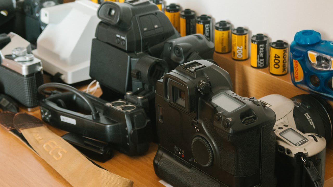 Vintage camera collection with various film rolls on a wooden desk.